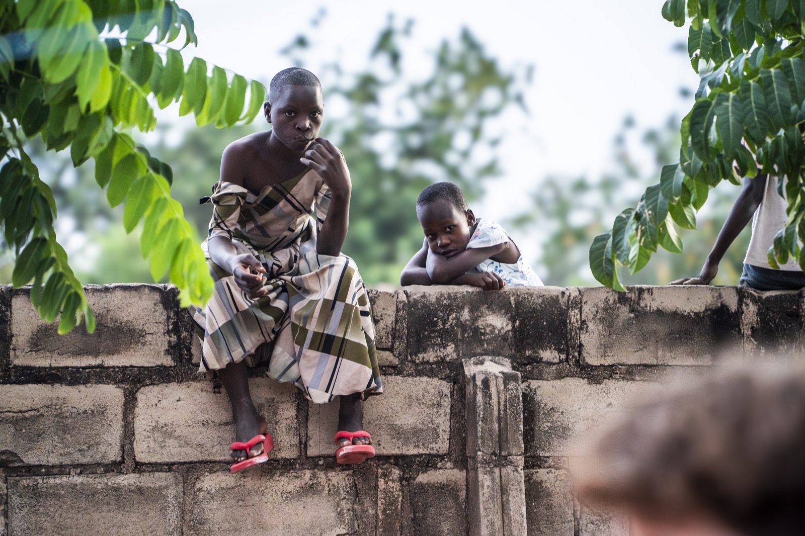 Children sitting outdoors in Tanzania under green leaves